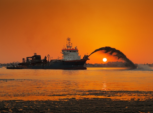 Barge dredging a channel at sunset.